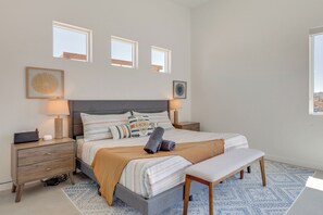 A bedroom with a bed, bedside tables, a bench, and two windows.