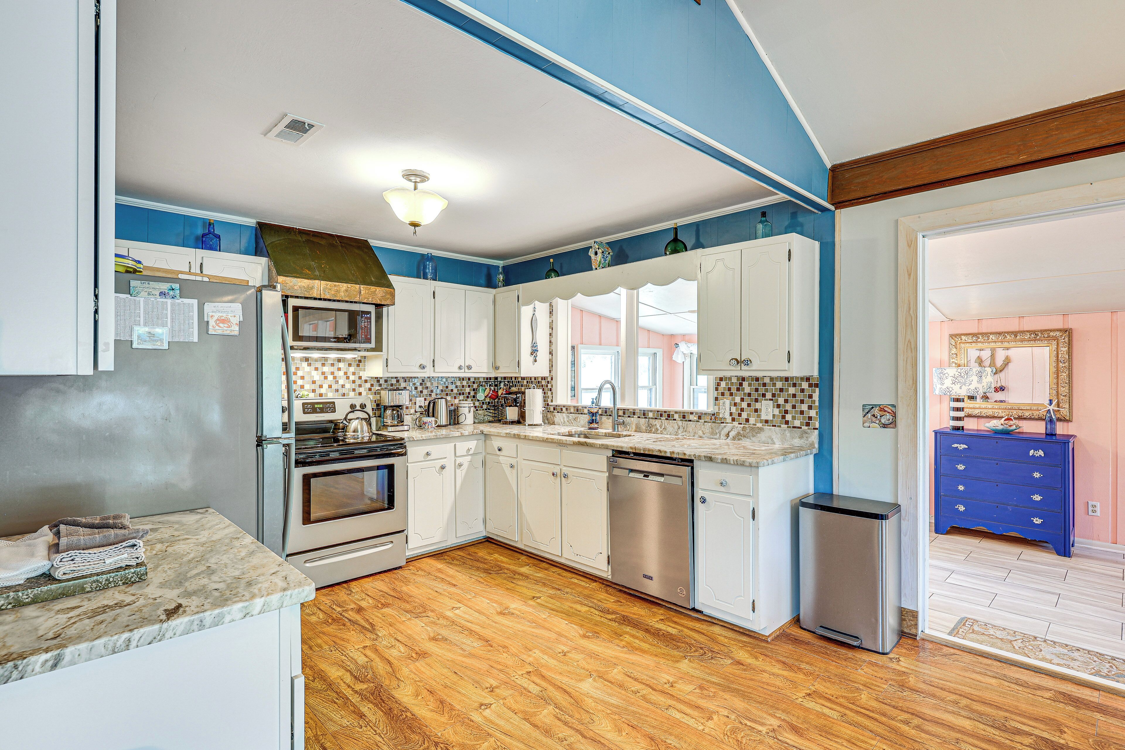 A kitchen with white cabinets, a stainless steel dishwasher, and a wooden floor.