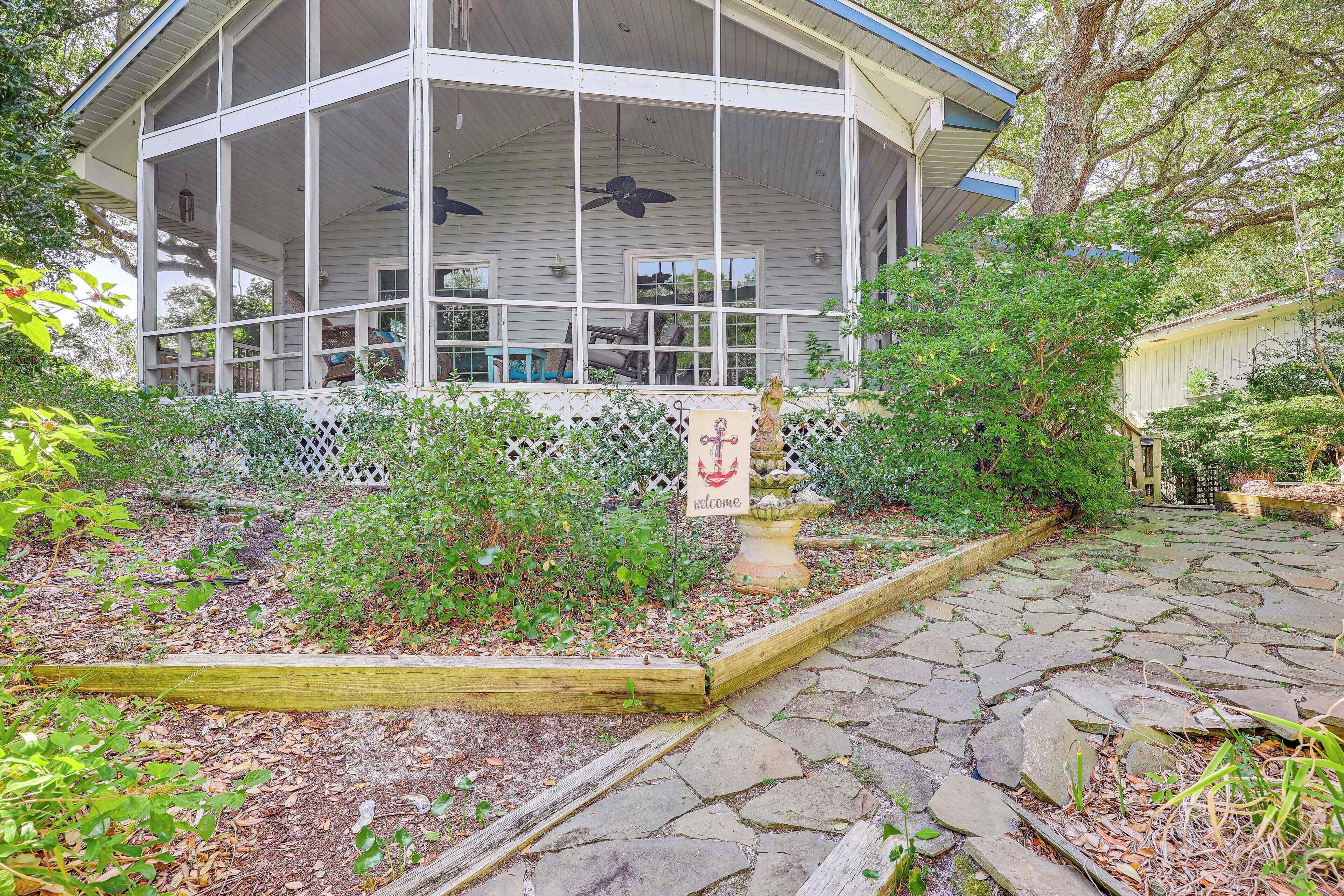 A covered porch with a white railing, a welcome sign, and a stone pathway leading to a building with large windows and a ceiling fan.