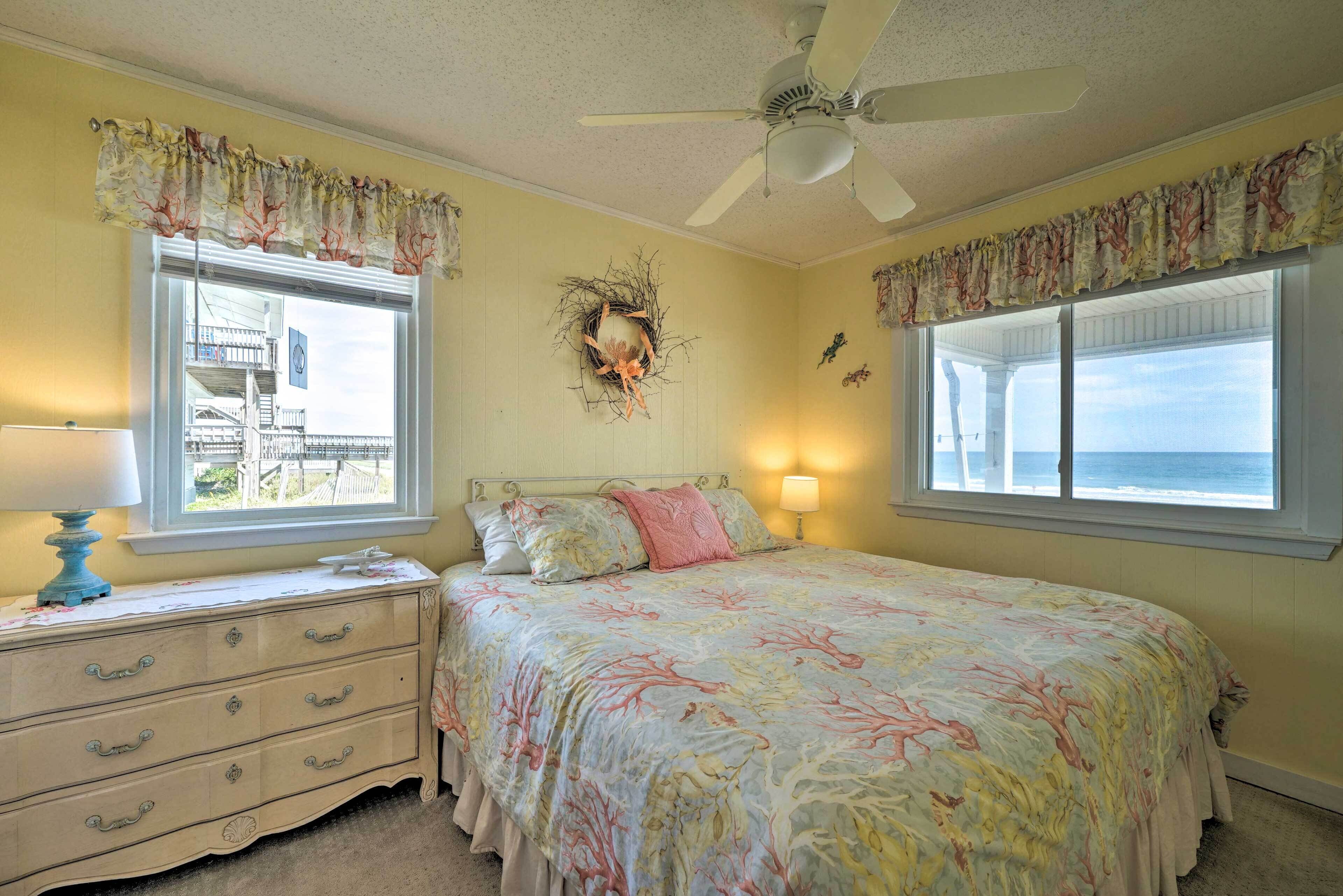 Une chambre à coucher comprenant un lit, une commode, deux fenêtres, un ventilateur de plafond et un élément décoratif mural.