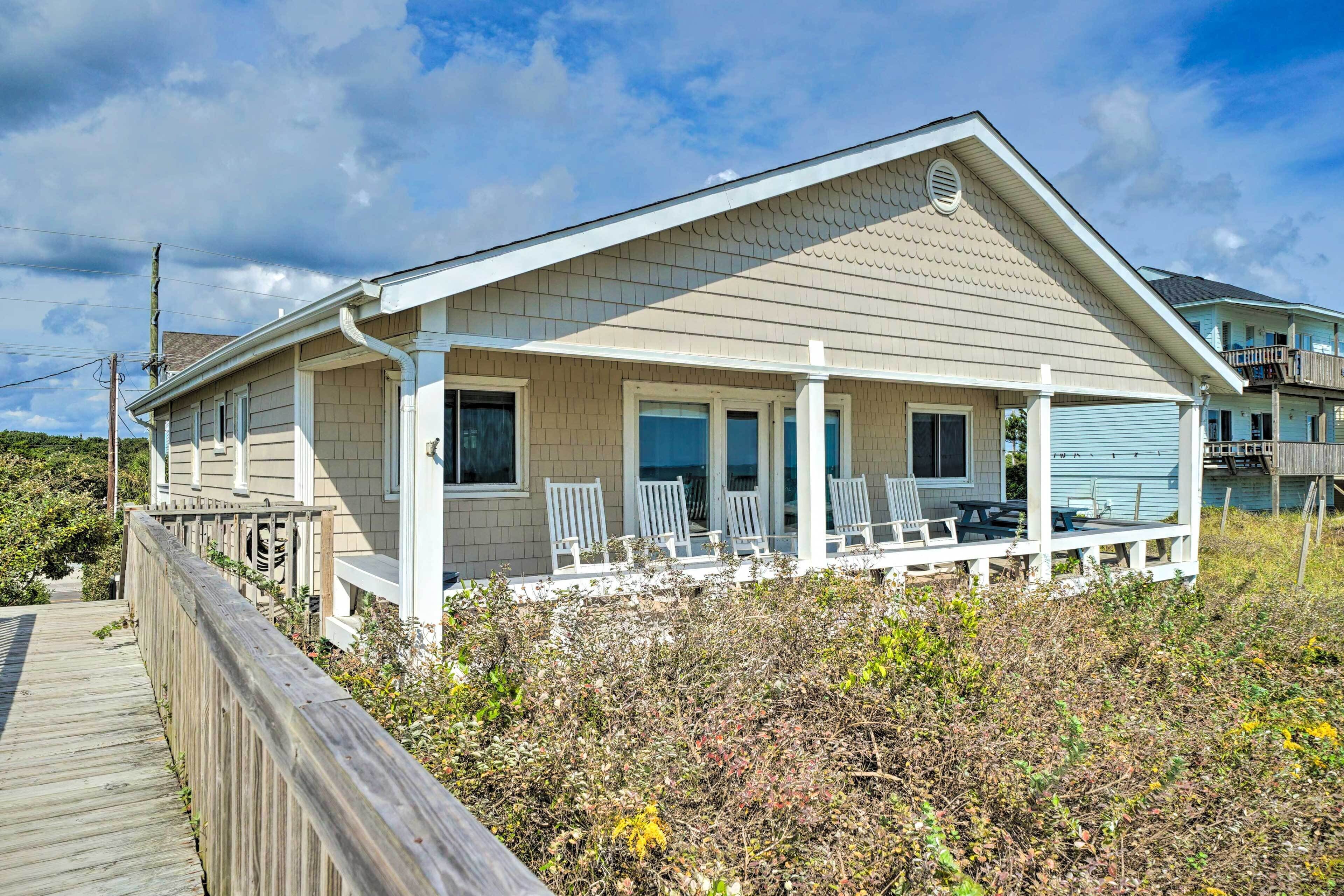 Une maison située en bord de mer, dotée d’un porche couvert, d’une terrasse en bois et offrant une vue sur l’océan.
