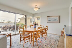 Un coin repas avec une grande table et des chaises en bois, un vase de fleurs et une vue sur l’océan grâce à de grandes portes-fenêtres coulissantes.