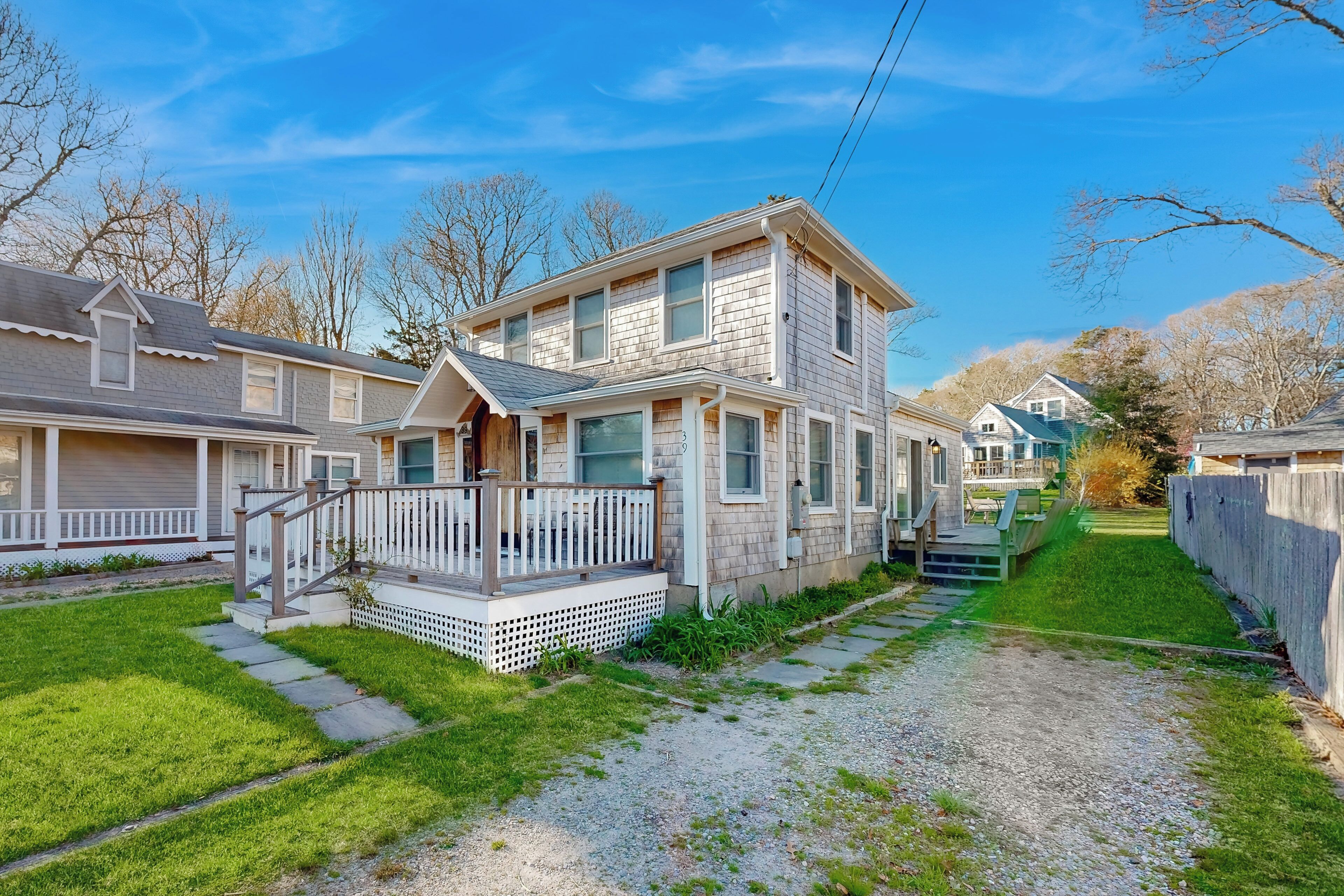 A two-story house with a front porch, a small deck, and a gravel driveway.