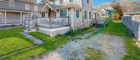 A two-story house with a front porch, a small deck, and a gravel driveway.