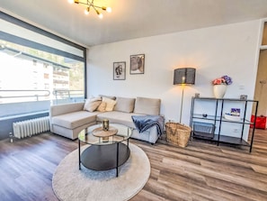 Ein modernes Wohnzimmer mit Ecksofa, Glastisch, Stehlampe und Blick ins Freie.