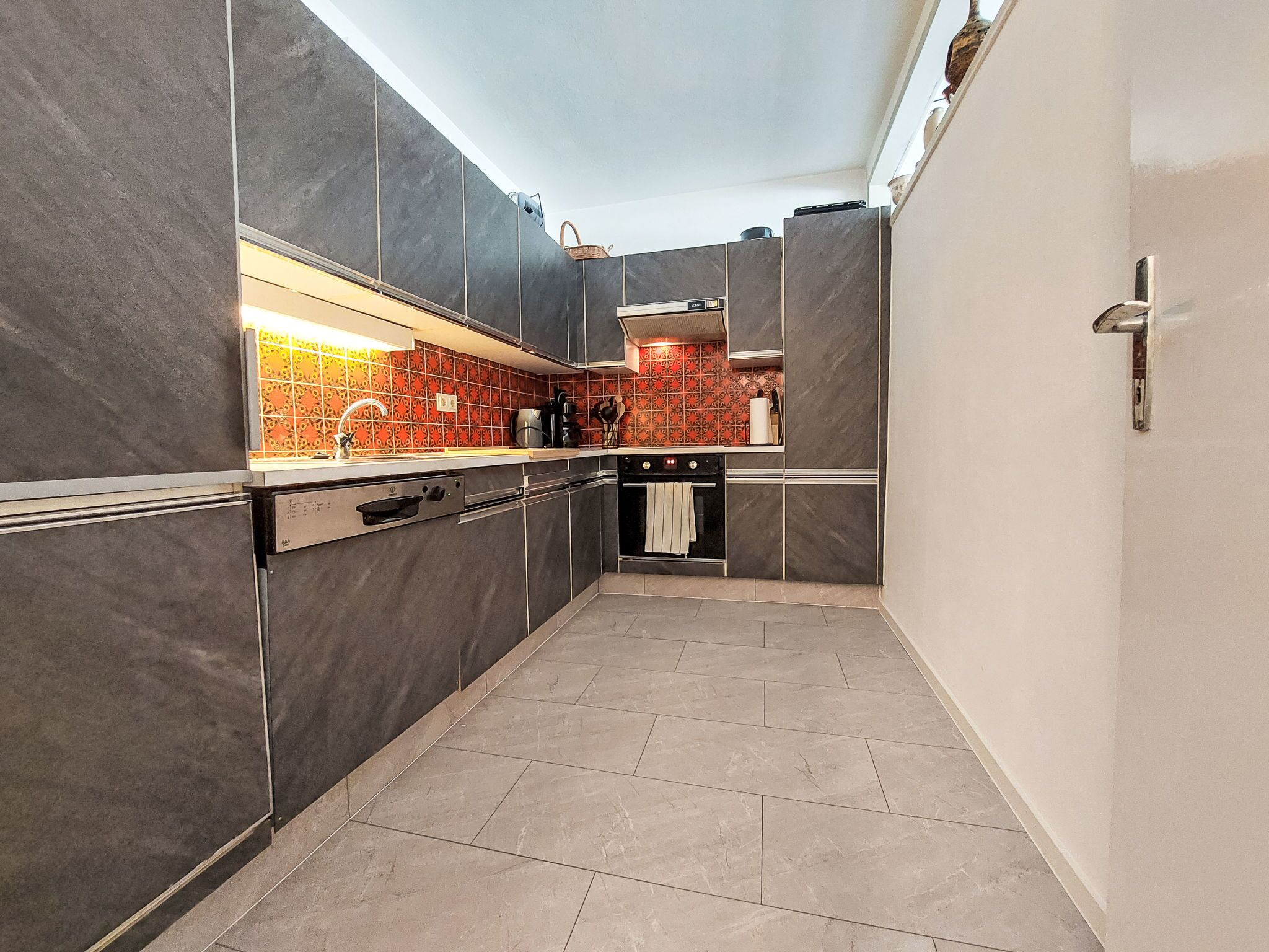 Uma cozinha moderna com armários escuros, painel de azulejos e forno embutido.