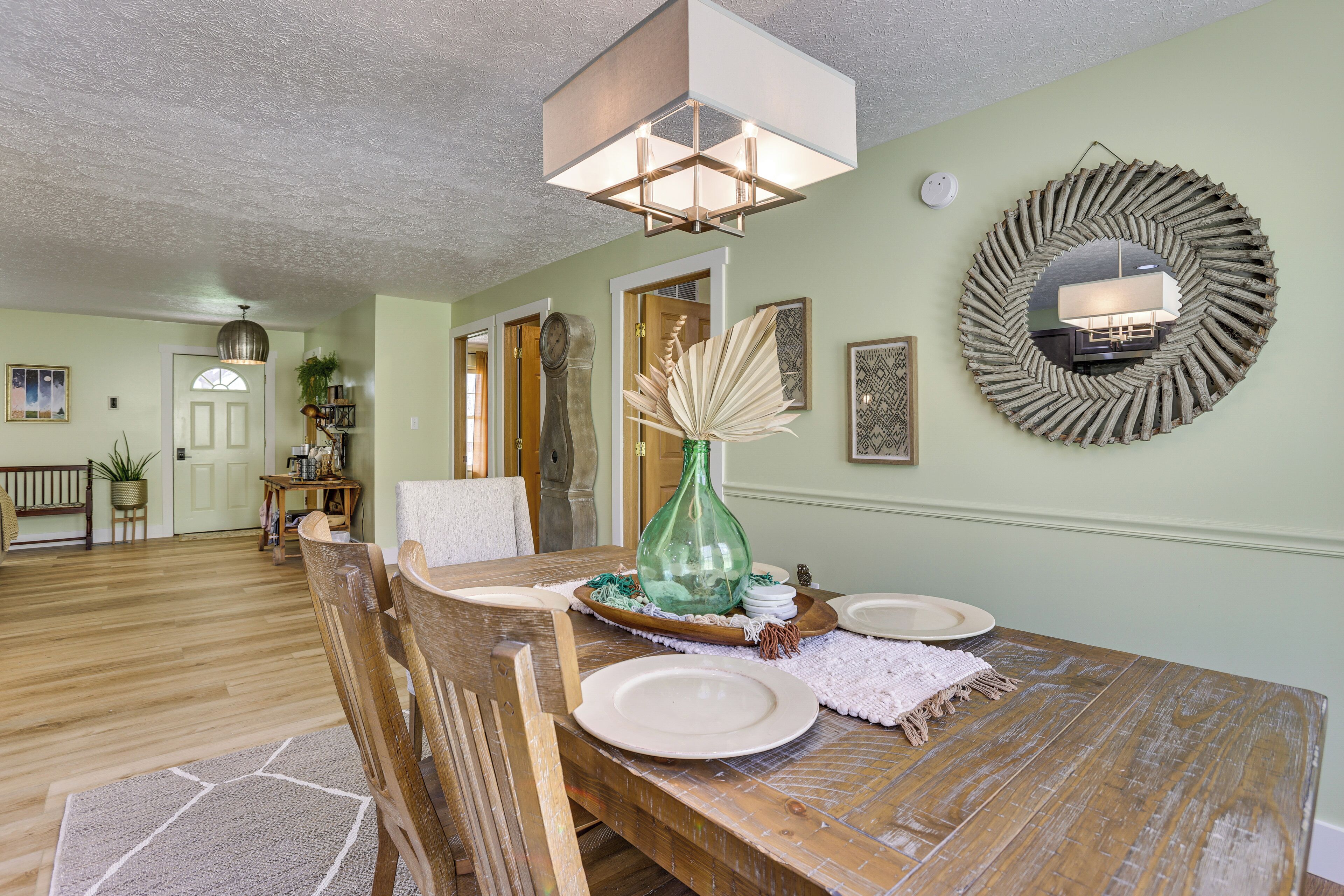 A dining area with a wooden table set for four, a green vase, and a mirror on the wall.