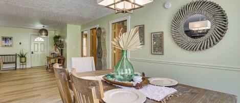 A dining area with a wooden table set for four, a green vase, and a mirror on the wall.