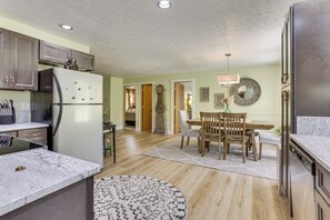 A kitchen with a refrigerator, wooden cabinets, a dining table with chairs, and a rug. - 'Be Still in the Hills' Laurelville Home, Hot Tub (Laurelville)