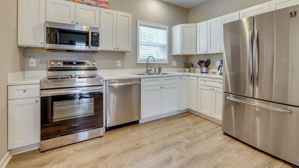 Una cocina moderna con armarios blancos, electrodomésticos de acero inoxidable y suelo de madera.