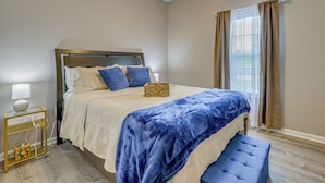 Un dormitorio con cama, mesita de noche, lámpara y ventana con cortinas.