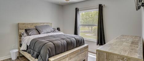 A bedroom with a bed, a ceiling fan, a window with curtains, and a wooden nightstand.