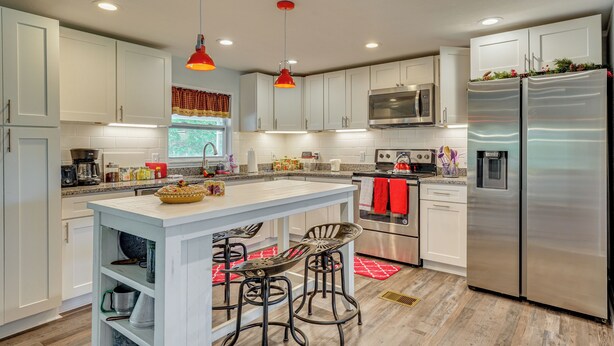 A modern kitchen with white cabinets, stainless steel appliances, and a central island with bar stools. - Quiet North Florida Charm Awaits (Mcalpin)