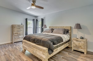 Quarto com cama de madeira, duas mesas de cabeceira, um ventilador de teto e vista pela janela.