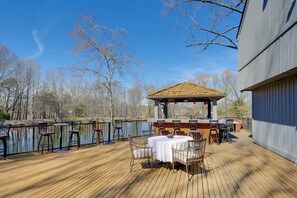 Eine Holzterrasse mit Außenmöbeln, einem Pavillon und Blick auf Bäume und ein Gewässer.