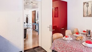 Un comedor con una mesa dispuesta para cuatro personas, una puerta roja y un perchero.