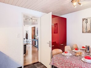 Un comedor con una mesa dispuesta para cuatro personas, una puerta roja y un perchero.