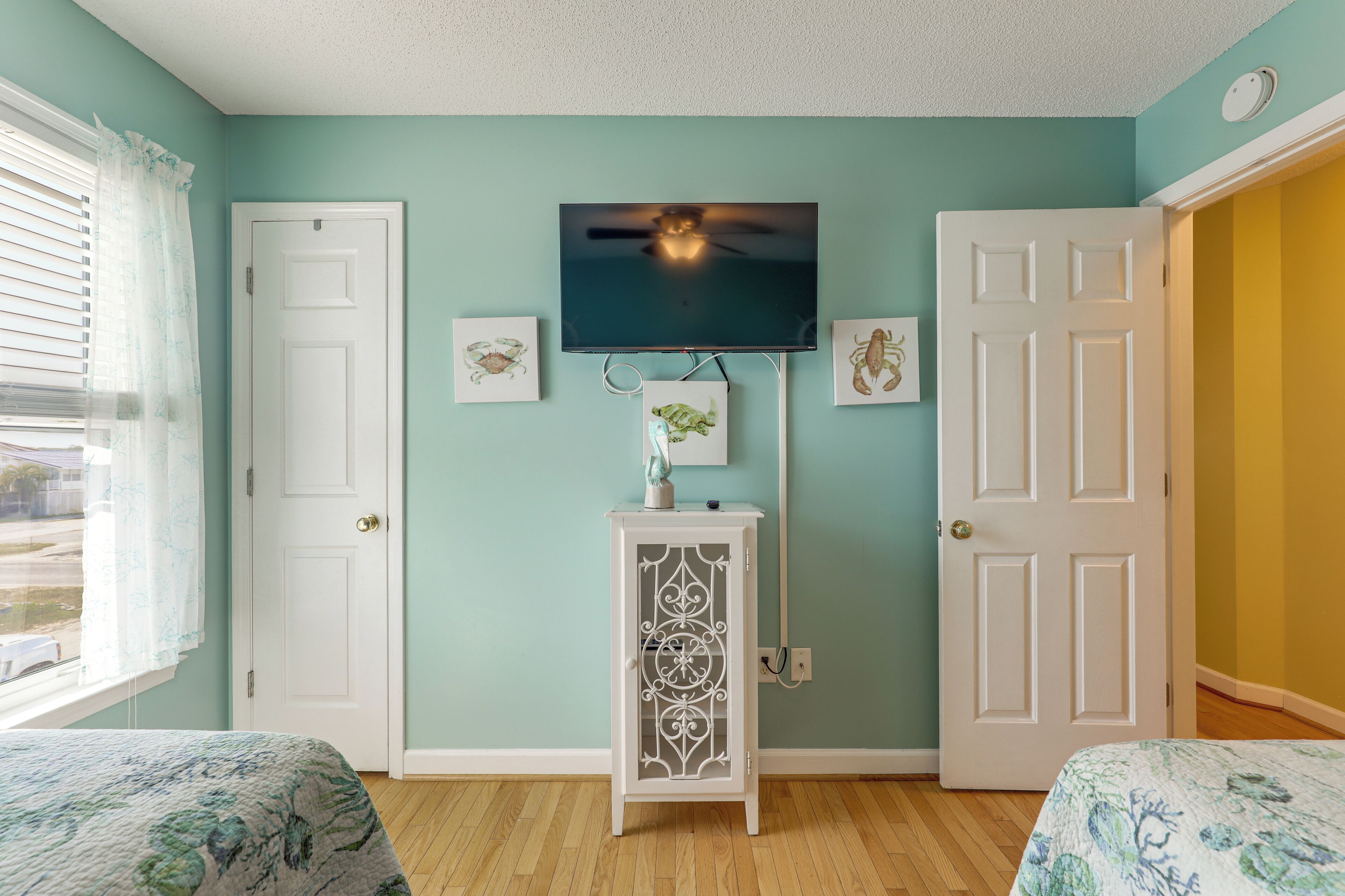 Un dormitorio con una cama, un televisor montado en la pared, un armario blanco y dos puertas.