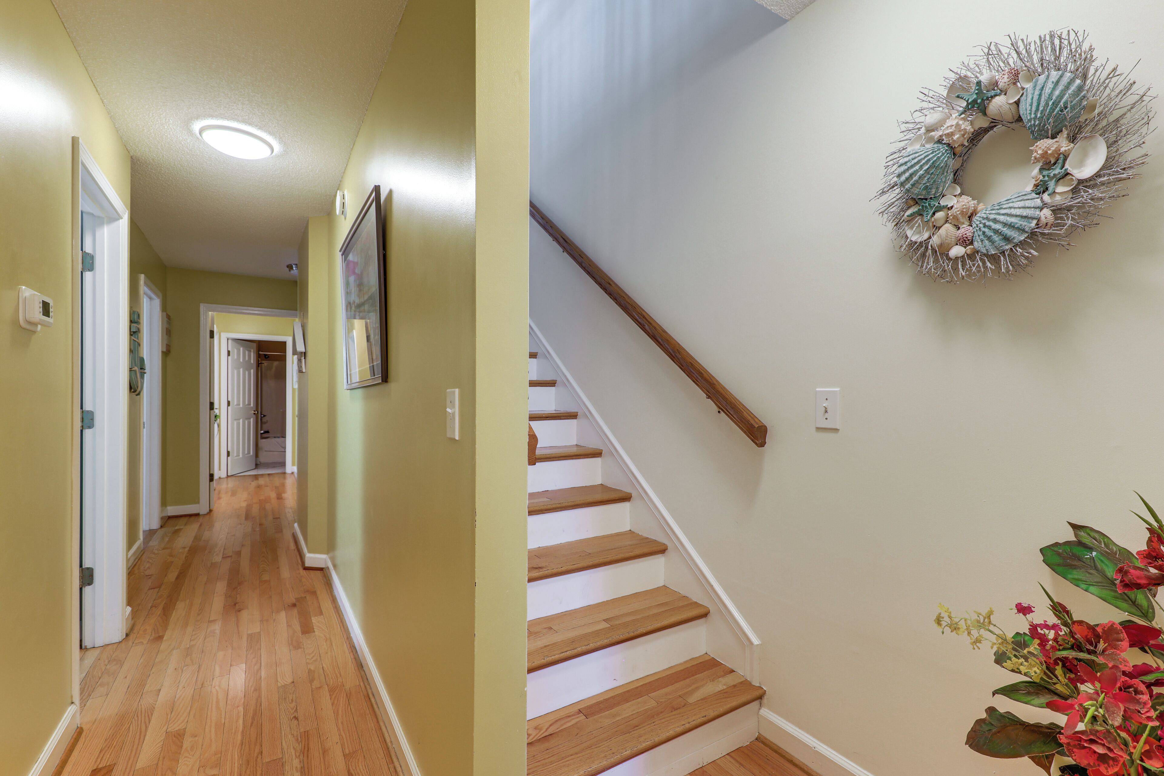 A hallway with wooden flooring and a staircase with a wooden handrail.