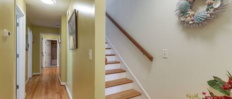 A hallway with wooden flooring and a staircase with a wooden handrail.