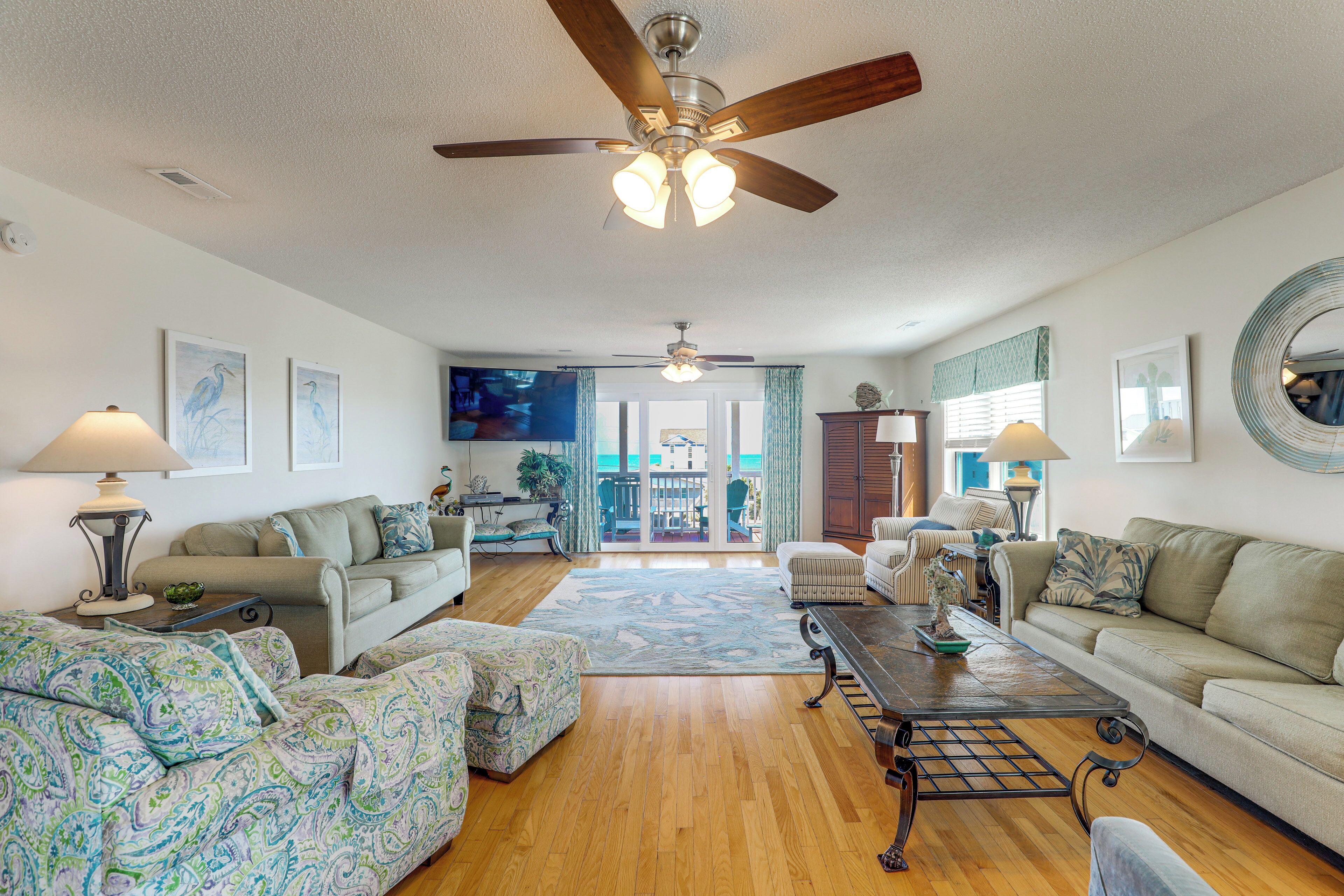 A spacious living room with a ceiling fan, a large TV, and a view to the outside.