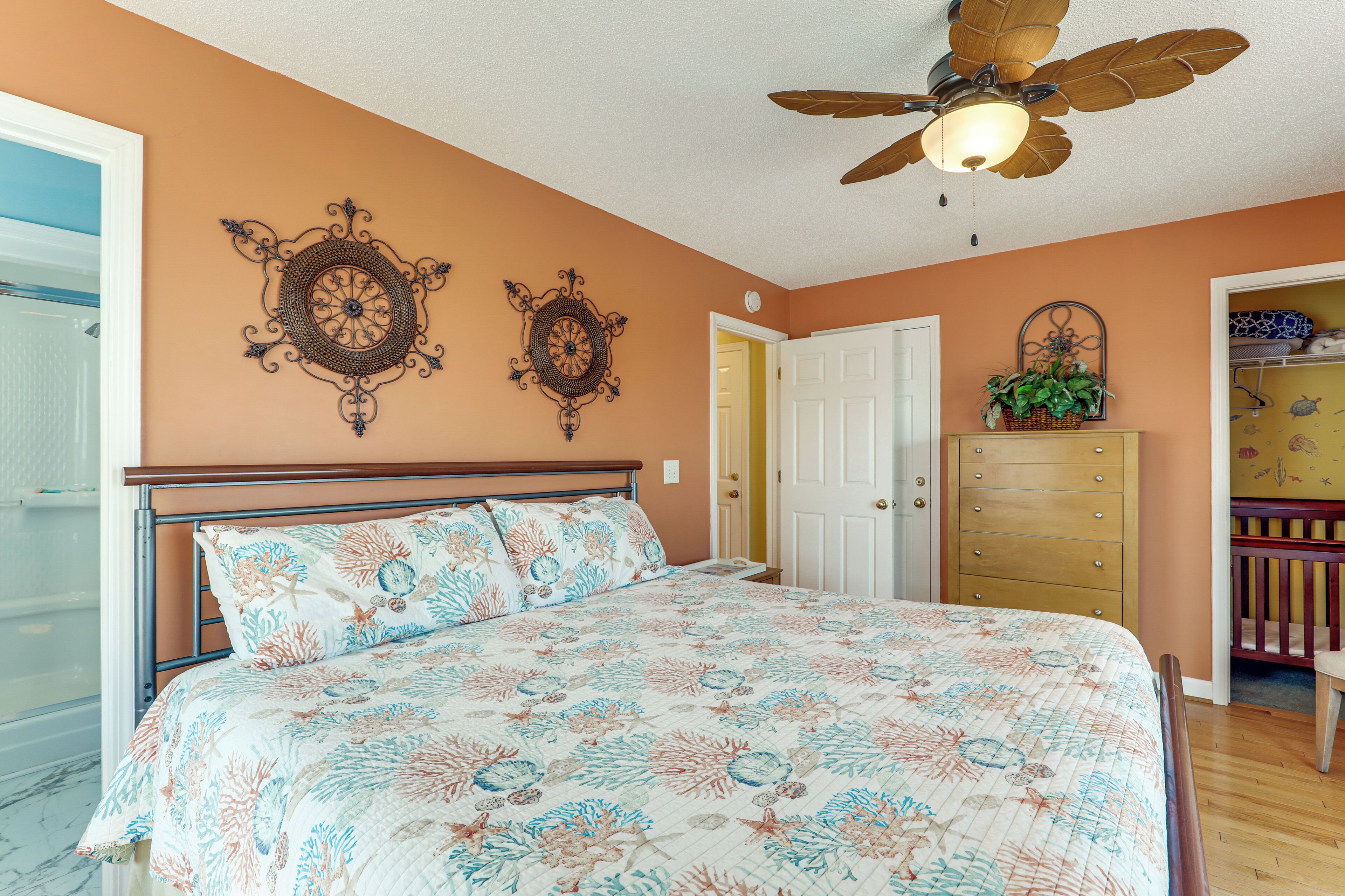 A bedroom with a bed, a ceiling fan, a dresser, and a door.