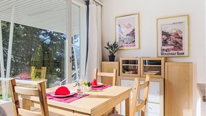 Ein Essbereich mit einem Tisch für zwei Personen, Holzstühlen, einer Topfpflanze und zwei gerahmten Bildern an der Wand.