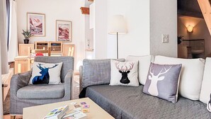 Ein modernes Wohnzimmer mit grauen Sofas, einem Couchtisch mit Zeitschriften und einer Treppe, die in einen oberen Bereich führt.