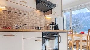 Eine moderne Küche mit eingebautem Ofen, Herd und Spüle. Durch ein großes Fenster ist ein Essbereich mit Tisch und Stühlen zu sehen.