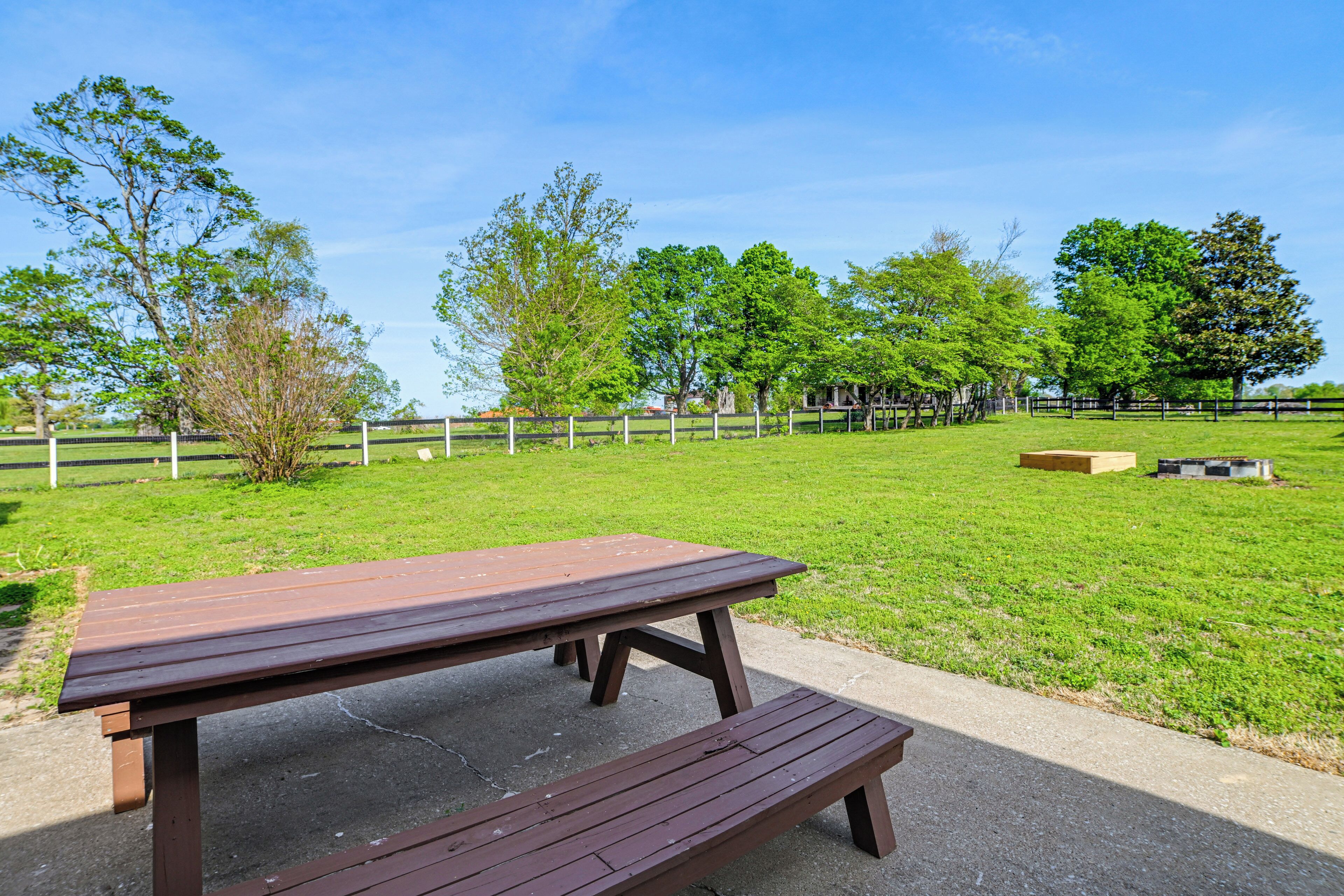A picnic table in a grassy park area with trees and a fence in the background.