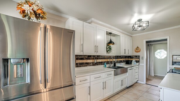 Cocina moderna con armarios blancos, un refrigerador de acero inoxidable, una lámpara colgante negra y un salpicadero de azulejos.