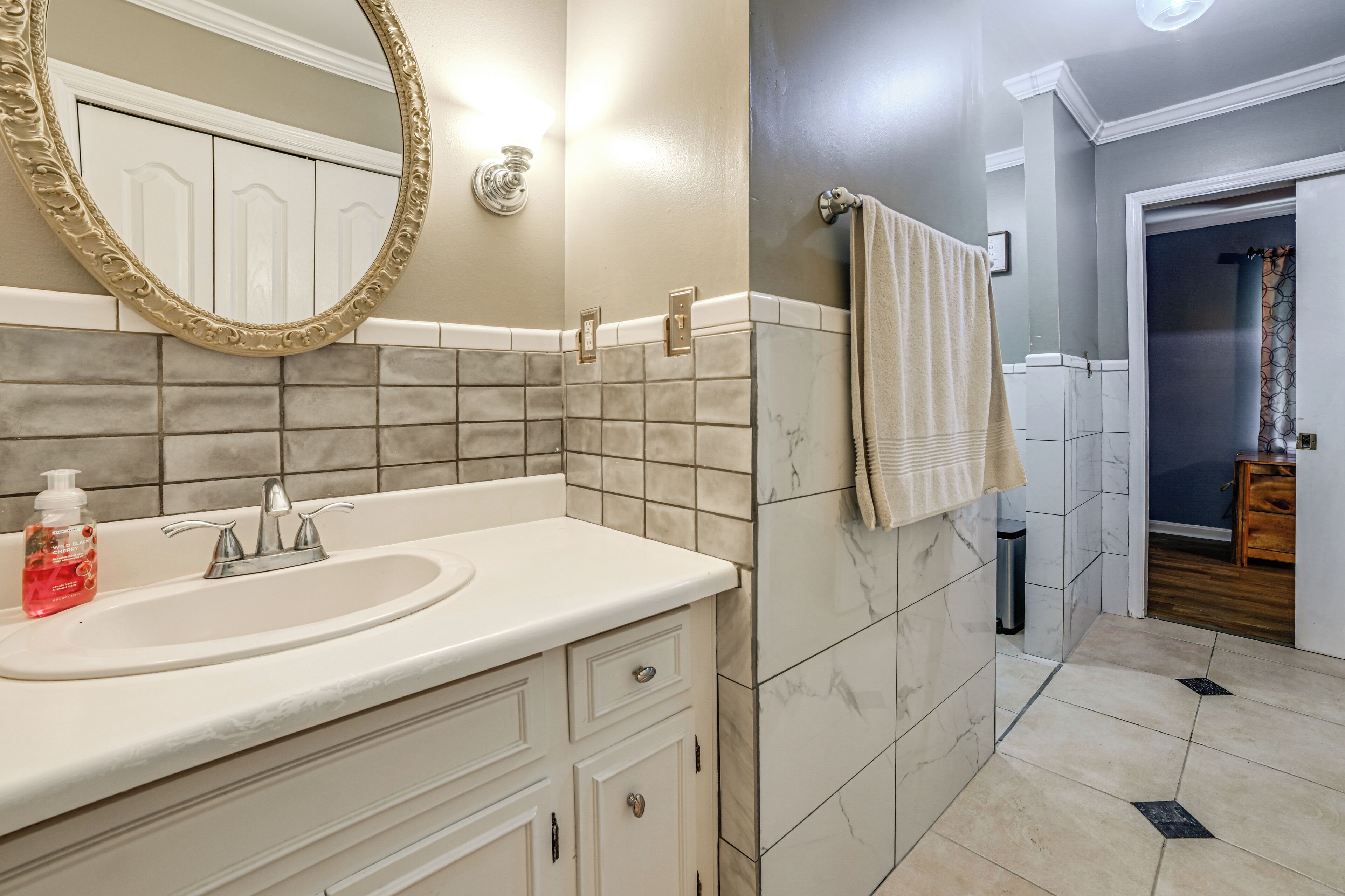 Un baño con lavamanos, espejo, perchero para toallas y paredes con azulejos.