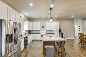 A modern kitchen with white cabinets, stainless steel appliances, a marble island, and a wooden floor.