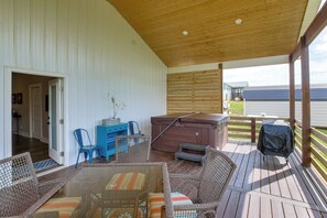 A covered deck with wicker furniture, a hot tub, and a barbecue grill.