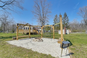 A wooden swing set, a wooden bench, and a small stone fire pit in a park area. - 'slate Drake Cabin' on Penns Creek w/ Deck & BBQ (Millmont)