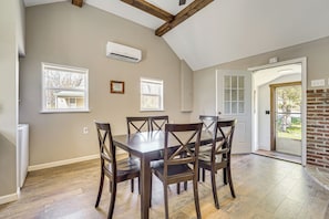 A dining area with a wooden table and chairs, a ceiling with exposed beams, and a view through a door to an outdoor area.