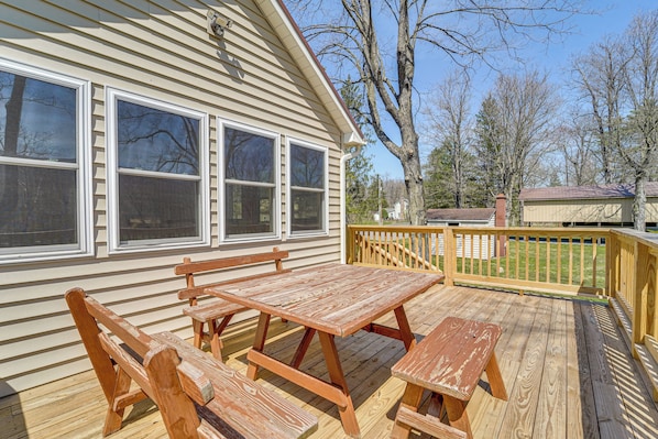 A wooden deck with a picnic table and benches, a wooden fence, and a house with large windows.