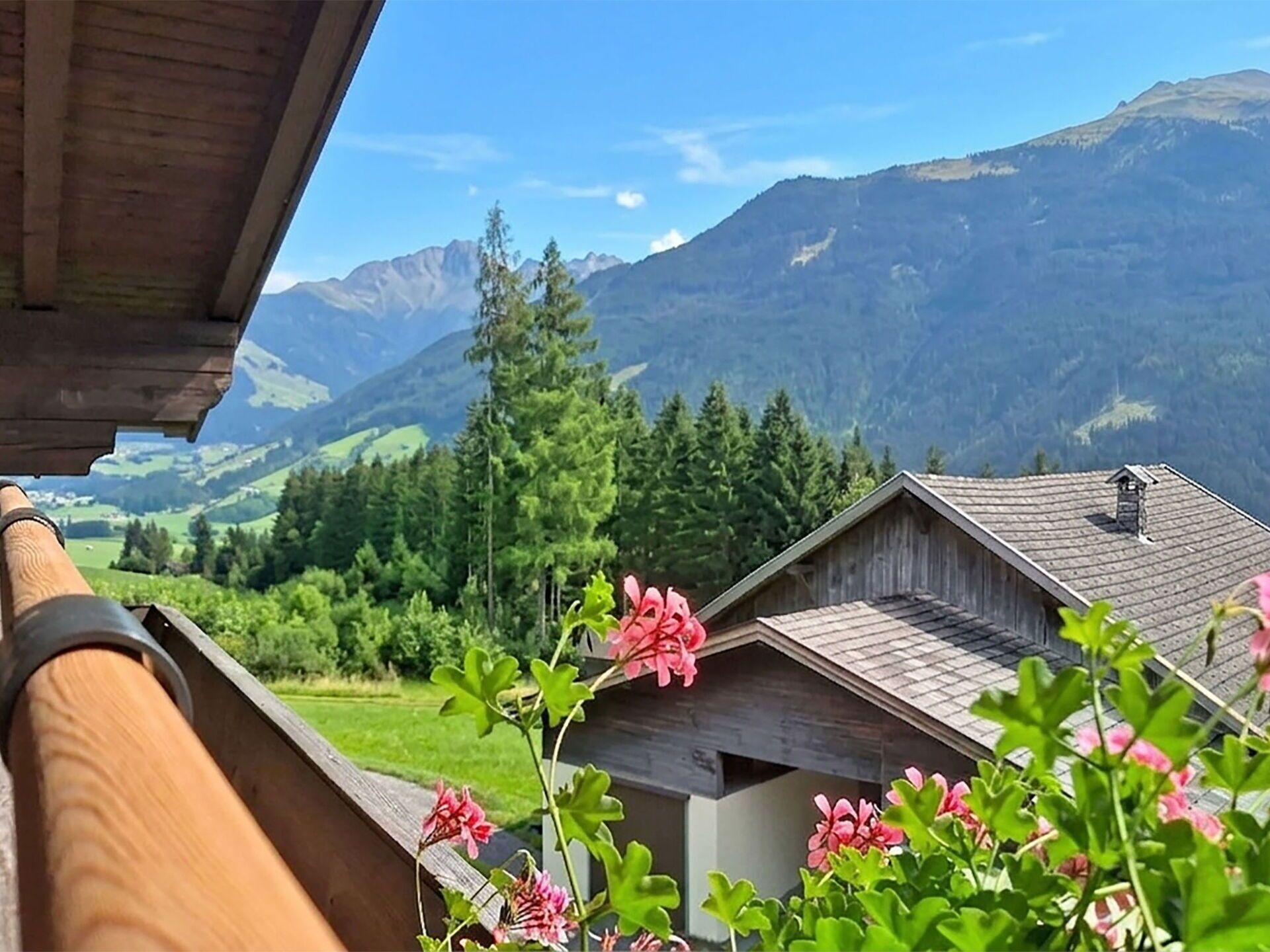 A wooden building with a sloped roof, surrounded by greenery and mountains in the background.