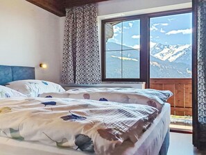 A bedroom with a bed, a window with a mountain view, and a patterned curtain.