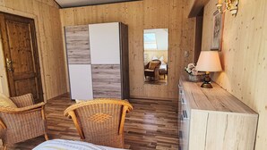 Une pièce comprenant un lit, deux fauteuils en osier, un bureau en bois, un miroir et une lampe.