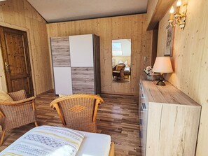 Ein Zimmer mit einem Bett, zwei Korbstühlen, einem Holztisch, einem Spiegel und einer Lampe.