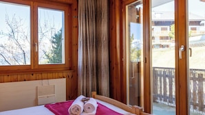 A wooden-paneled room with a bed, a window, and a sliding glass door to a balcony. - Beautiful apartment for 5 people with TV and balcony (Veysonnaz)
