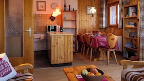 A cozy kitchen with wooden cabinets, a dining table set for four, and a small island with a microwave. - Beautiful apartment for 5 people with TV and balcony (Veysonnaz)