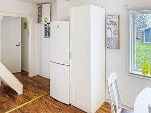 Eine kompakte Küche mit einem weißen Kühlschrank, Holzboden, einem Fenster mit Blick auf Grünflächen und einer Tür zu einem anderen Raum.