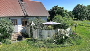 Une maison avec un toit rouge, une clôture blanche en bois et un jardin où poussent différentes espèces de plantes.