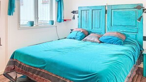 Un lit avec une couvre-lit turquoise et des bordures marron, une fenêtre avec des rideaux, une lampe et une porte bleue.