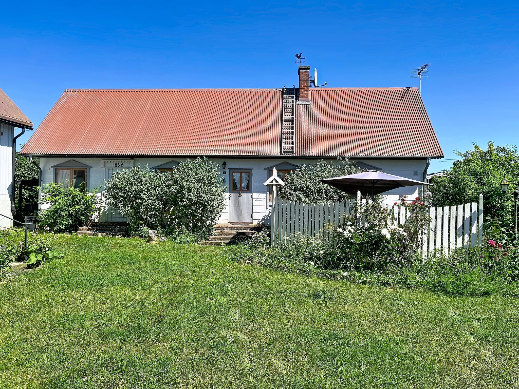 A two-story house with a red roof, a white picket fence, and a small porch.