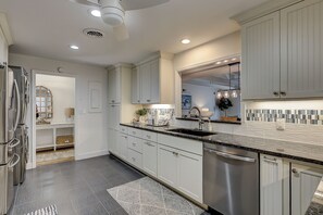 A modern kitchen with stainless steel appliances, white cabinetry, and a black granite countertop. - Sunset Rentals | Queens Grant 684 | Dog Friendly (Hilton Head Island)