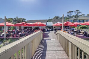 An outdoor dining area with red umbrellas and tables, a wooden deck, and a view of the building in the background. - Sunset Rentals | Queens Grant 684 | Dog Friendly (Hilton Head Island)