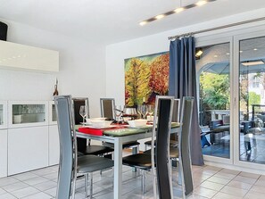 A modern dining area with a glass table, metal chairs, and a painting of trees.